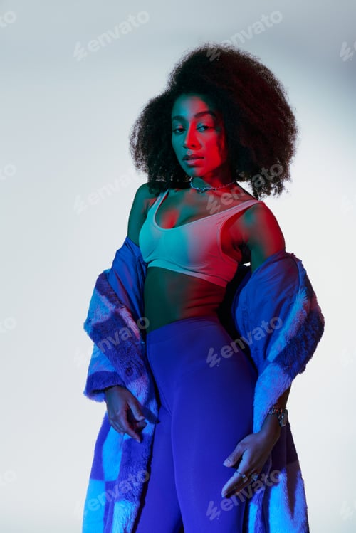 Preview: appealing sexy african american woman in fashionable stylish faux fur looking at camera in lights