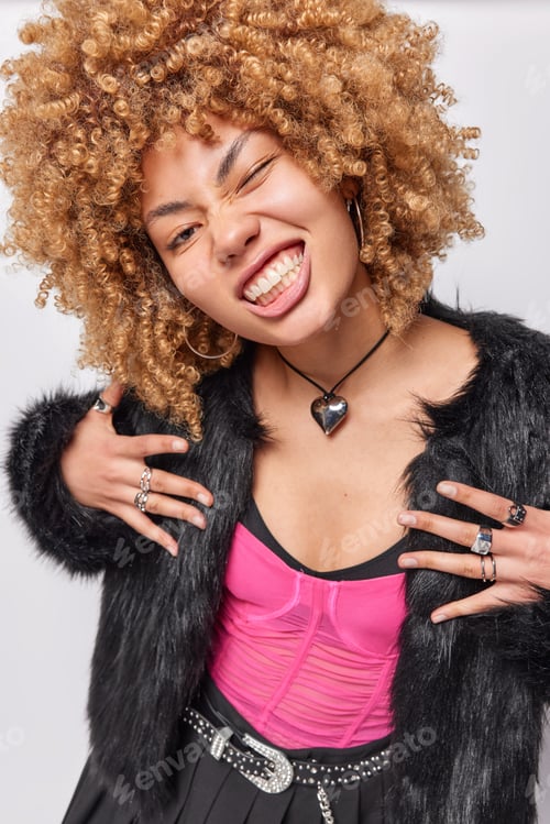 Preview: Vertical image of funny curly haired woman winks eye and clenches teeth has playful expression
