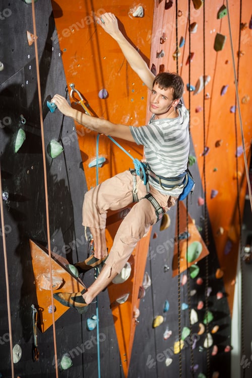 Preview: Male rock-climber practicing climbing on rock wall indoors