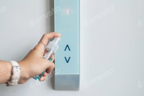 Preview: Woman hand spraying alcohol sanitizer bottle to the button control of elevator, against coronavirus