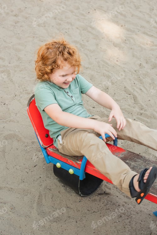 Preview: high angle view of cheerful boy riding seesaw in amusement park