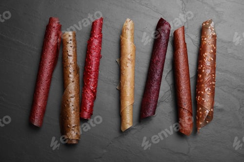 Preview: Delicious fruit leather rolls on black table, flat lay