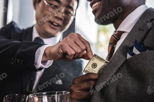 Preview: Cropped shot of two smiling businessmen talking and holding dollar banknote