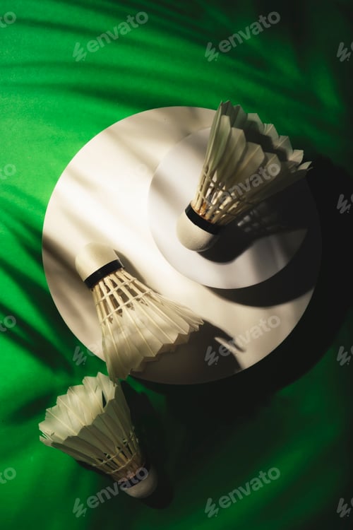 Preview: shuttlecocks for badminton game on green background with hard light and shadows from palm tree