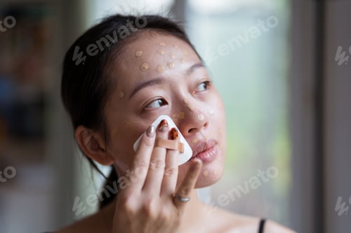 Preview: Satisfied Asian visagiste applying foundation cream on face