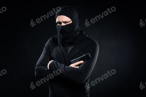 Preview: Thief in black balaclava holding gun in folded arms on black