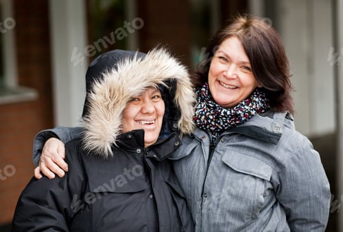 Preview: Portrait of happy caregiver with mentally disabled woman in warm clothing outdoors