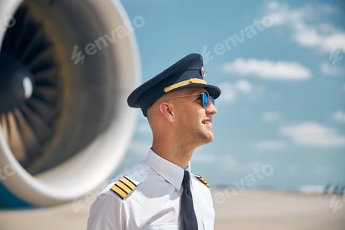 Preview: Cheerful pilot in sunglasses standing outdoors in airfield