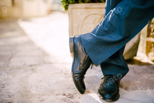 Preview: Male feet in black shoes and blue trousers on the stone floor. Close-up