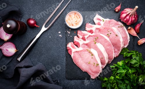 Preview: Raw pork chops on slate board prepared for cooking with spices and pepper. Black kitchen table
