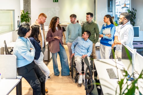 Preview: Diverse business team discussing in modern office with disabled colleague in wheelchair