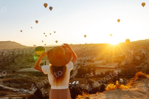 Preview: Woman stands on mountain with flying air balloons on background. Tourist Turkish region Cappadocia.