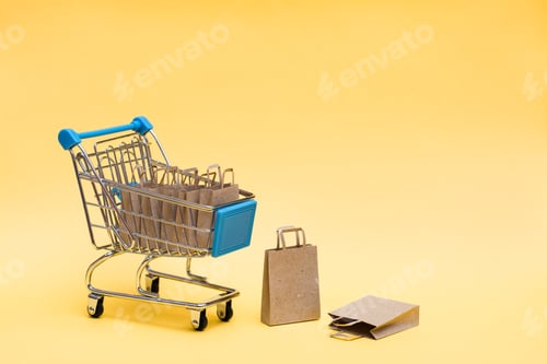 Preview: Eco-friendly kraft paper shopping bags in and next to a shopping cart on a yellow background.