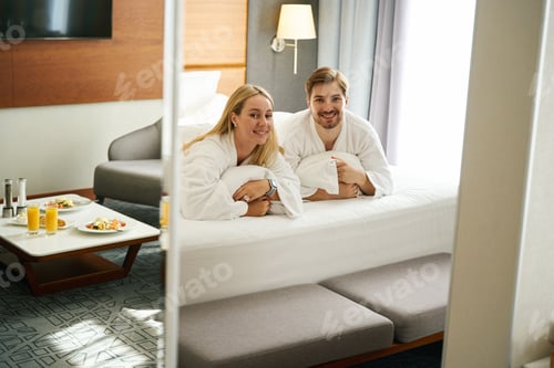 Preview: Happy newlyweds are seated on pillows on a large bed