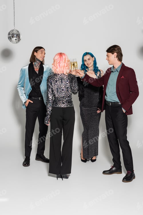 Preview: full length of stylish nonbinary friends clinking champagne glasses on grey background