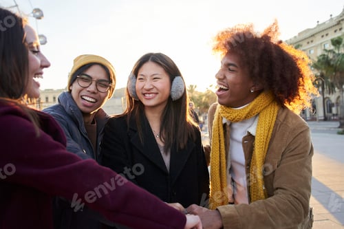 Preview: Group of cheerful multiracial friends bump fists with a smile at amusement park in winter season.