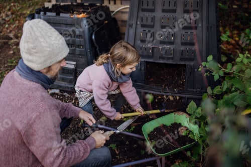 Preview: Girl helping father to remove compost from a composter in garden. Concept of composting and