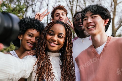 Preview: Joyful diverse group of friends taking a selfie outdoors with trees and urban background.