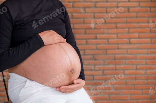 Preview: Mom pregnant woman in a dress holds hands on belly on red brick background, Waiting for the birth