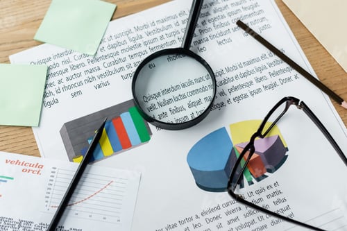 Preview: top view of magnifier and glasses on charts near stationery on desk