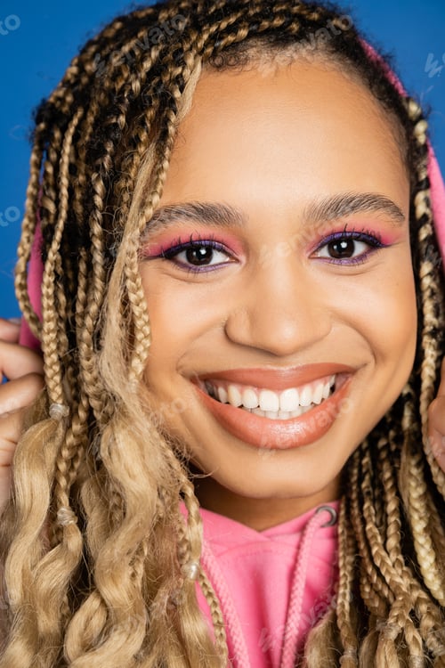 Preview: close up of cheerful black woman with hood on head looking at camera and smiling on blue background