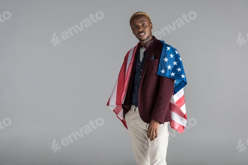 Preview: african american man with american flag on shoulders looking at camera isolated on grey