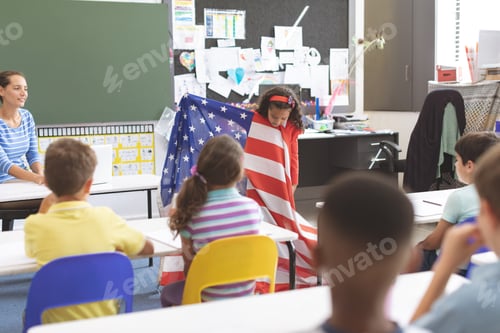 Preview: Mixed-race schoolgirl holding american flag in classroom at school while his classmates are sitting