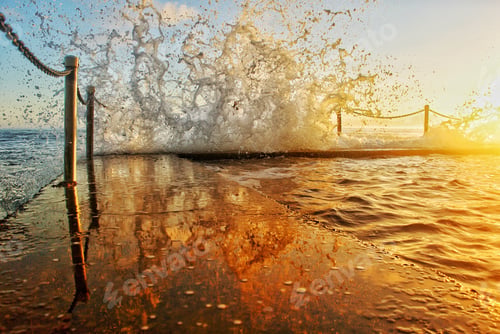 Preview: Golden reflections of a wave splashing on the edge of an ocean pool