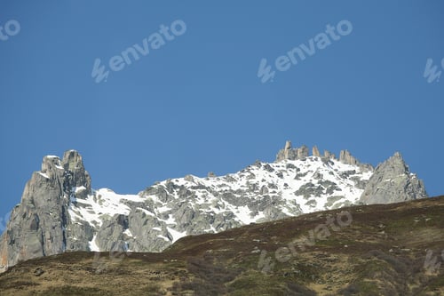 Preview: Snow-capped mountain peaks under a clear blue sky, showcasing rugged terrain and natural beauty.