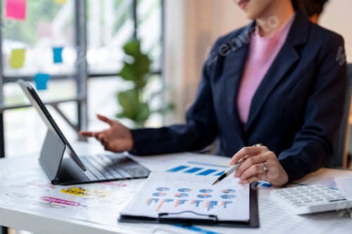 Preview: A woman in a business suit is sitting at a desk with a laptop and a clipboard