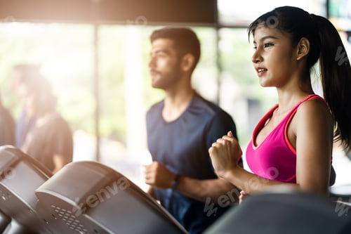 Preview: Asian female athlete jogging on treadmill or running machine with Caucasian man in gym or fitness.