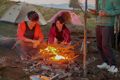 Preview: Young happy couple of travelers sitting at fire in evening at camping place. Romantic moment.
