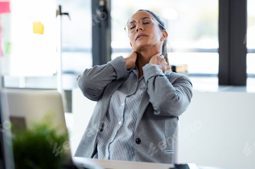 Preview: Tired young woman with neck pain working with her computer in the office