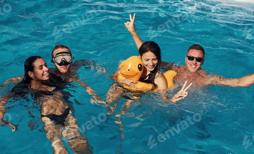 Preview: Using yellow colored duck to swim. Group of young happy people have fun in swimming pool at daytime