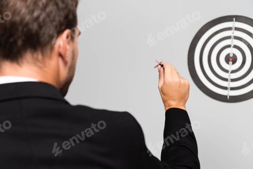 Preview: back view of businessman in suit playing darts isolated on grey