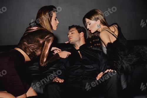Preview: attractive and stylish women holding tie of handsome man isolated on black