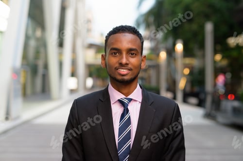 Preview: Portrait of handsome young African businessman smiling outdoors in city
