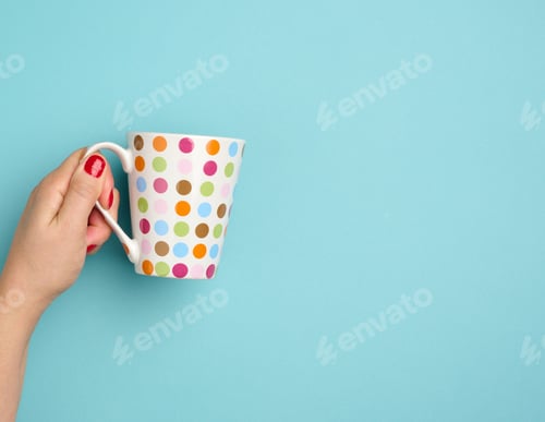 Preview: Female hand holds a ceramic mug on a blue background, break time and drink coffee