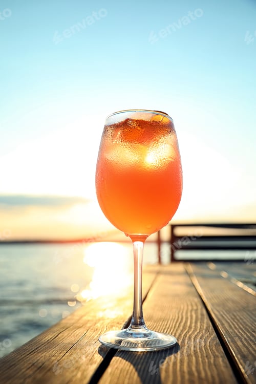 Preview: Glass of fresh summer cocktail on wooden table outdoors at sunset