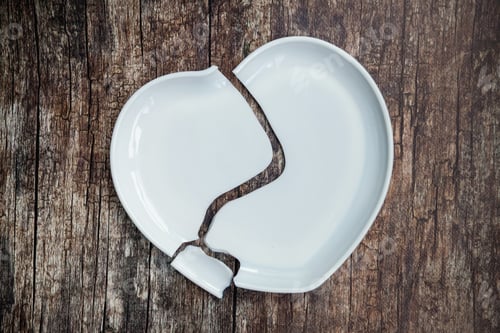 Preview: Broken white ceramic plate in shape heart on wooden floor background