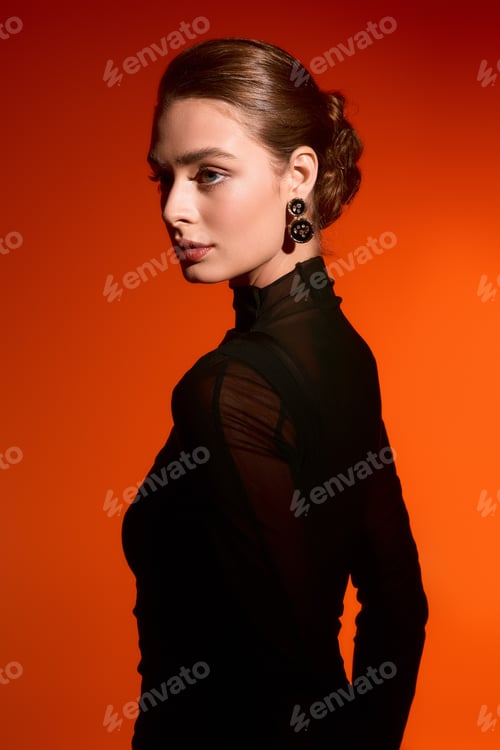 Preview: Elegant woman in a chic outfit with striking features against a warm orange backdrop