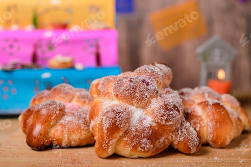 Preview: Pan de muertos on wooden table with altar in the background.