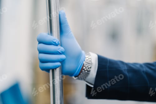 Preview: Mans hand in blue disposable glove touching handrail in public transport. Pandemic precaution