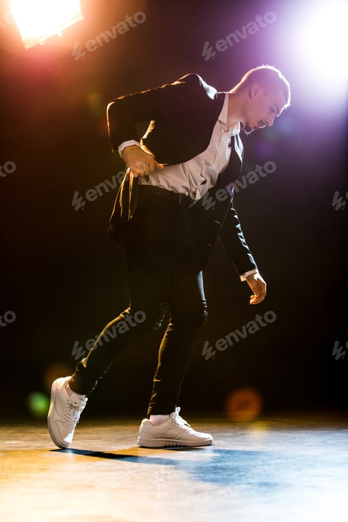 Preview: Full length portrait of handsome stylish man in black suit dancing under spotlights