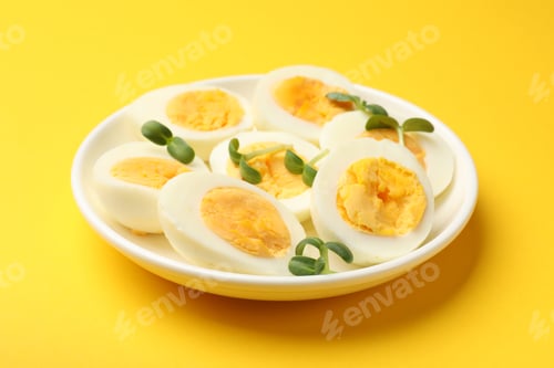 Preview: Halves of hard boiled eggs with microgreens on yellow background, closeup