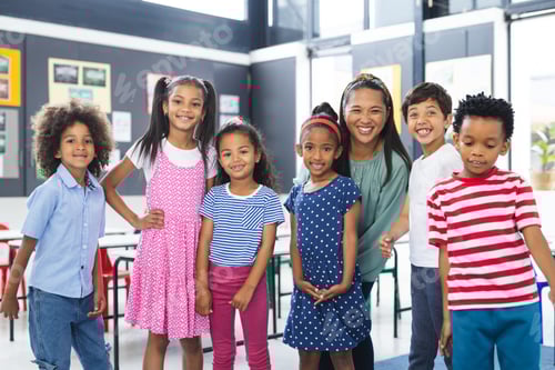 Preview: In school, middle-aged biracial teacher smiles with her young students in the classroom