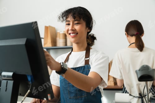 Preview: woman cashier wears an apron and using pos terminal to input orders on coffee shop counter.