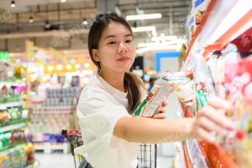 Preview: Young adult woman using phone in grocery store
