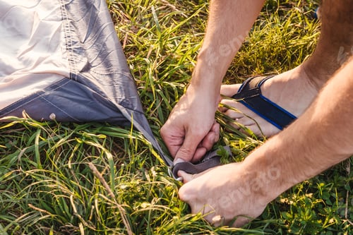Preview: Closeup of male hands pegging down tent.