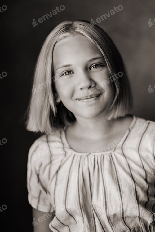 Vorschau: Ein glückliches Kind, ein kleines Mädchen in einem grauen T-Shirt auf beigem Hintergrund. Schwarz-Weiß-Foto